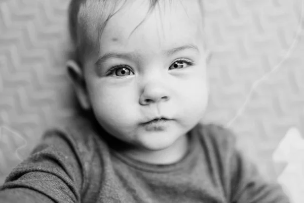 Un pequeño bebé con un traje blanco está acostado en una alfombra. Retrato. Primer plano. Foto en blanco y negro — Foto de Stock