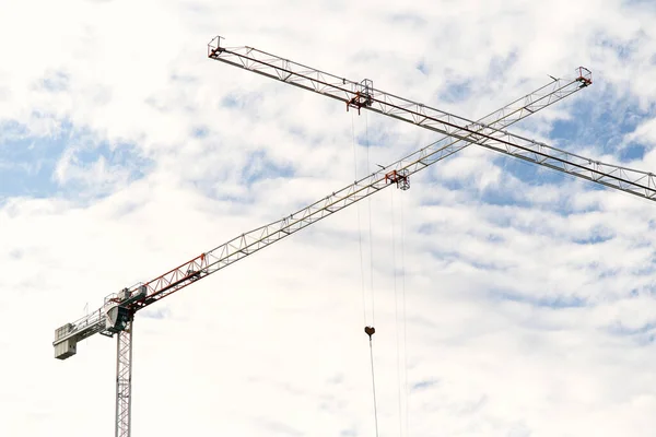 Two tower cranes with crossed booms at a construction site against a blue sky with white clouds — Stock Photo, Image