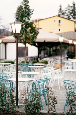 Açık hava restoranı. Hasır sandalyeler ve masalar evin arka planında parlayan fenerlerin yanında duruyor.