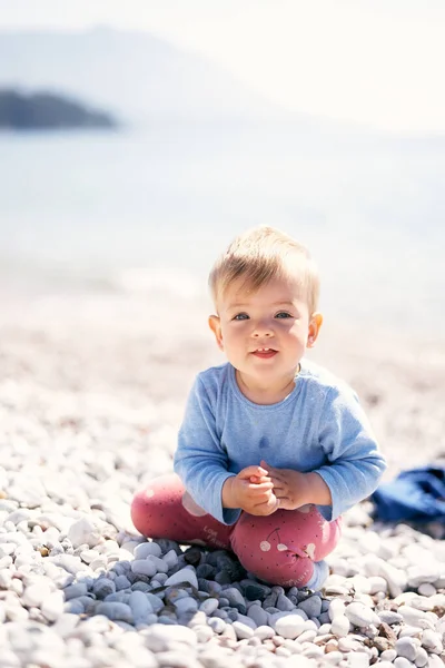 아장아장 걷는 아기는 자갈 해변에 무릎을 꿇고 앉아 있다. 클로즈업 — 스톡 사진