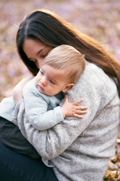 Mamãe abraça o bebê no peito e o beija, sentado na folhagem do parque. Close-up — Fotografia de Stock