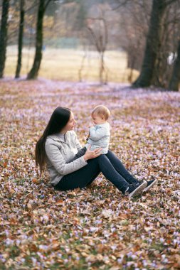 Annem parkta düşmüş yapraklara oturur, bebeği kucağında tutar, onunla yüz yüze oturur.