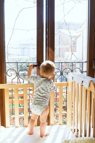 Anak kecil membuka pintu balkon, berdiri di tempat tidur kayu. Tampilan belakang — Stok Foto