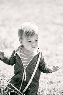 Tulumlu küçük bir çocuk çimlerin üzerinde dizlerinin üzerinde oturuyor. Siyah beyaz fotoğraf. Yakın plan.