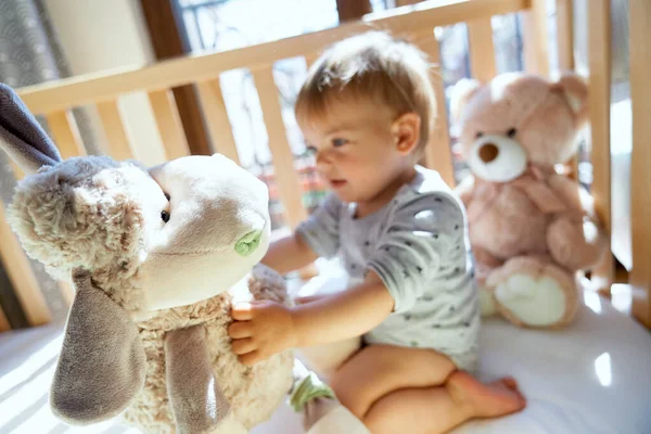 Tersenyum anak kecil duduk di tempat tidur kayu dan memegang domba besar yang mewah — Stok Foto