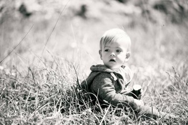 Tulumlu küçük bir çocuk çimlerin üzerinde oturuyor. Siyah beyaz fotoğraf. Yakın plan.