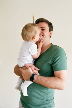 Küçük kız kollarında otururken gülümseyen babasını öpüyor.