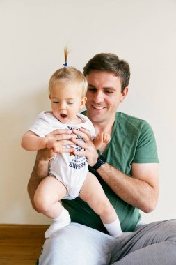 Gülümseyen baba kollarında şaşkın bir kız tutuyor.