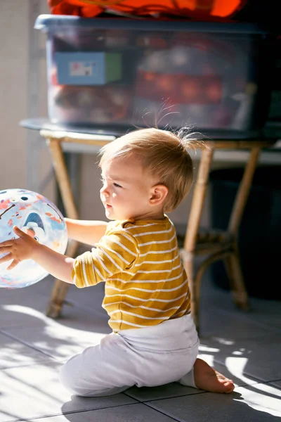 Anak kecil duduk berlutut di balkon dan memegang bola di tangannya — Stok Foto