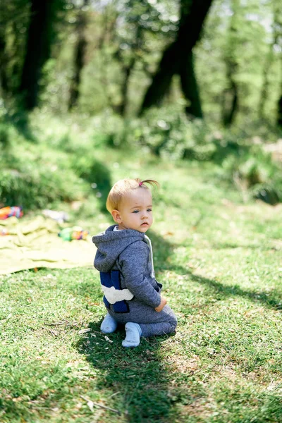 Liten flicka i overall knäböjer på en grön gräsmatta — Stockfoto