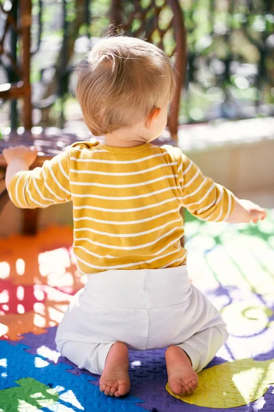 Anak kecil yang berlutut di karpet berwarna di balkon. Tampilan belakang — Stok Foto