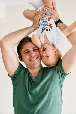 Gülümseyen baba baş aşağı küçük gülen kızı tutuyor.