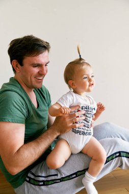 Gülümseyen baba kucağında at kuyruğu olan küçük bir bebek tutuyor.