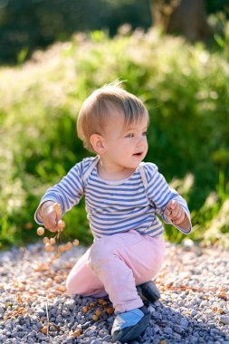 Çocuk dizlerinin üstüne çöküp böğürtlenli bir dal tutuyor.