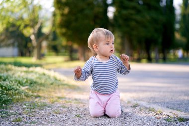 Küçük çocuk parkta dizlerinin üzerinde oturuyor.