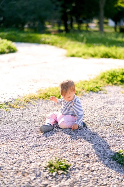 Liten unge som sitter på en grusgång i parken — Stockfoto