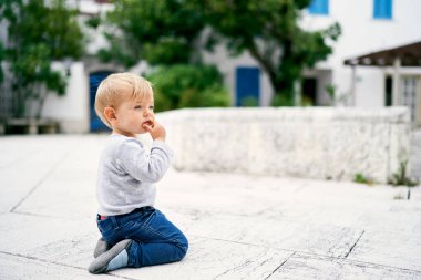 Düşünceli çocuk bir binanın arka planında dizlerinin üzerinde oturuyor.