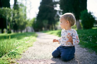 Yürümeye başlayan çocuk yeşil parkın ortasında dizlerinin üzerinde oturuyor.