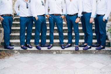 Seven grooms best men in identical blue trousers and shoes stand on the stairs, close-up 
