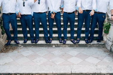 Seven grooms best men in identical blue trousers and shoes stand on the stairs, close-up 