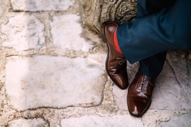Crossed legs of a man in blue pants, red socks and brown shoes standing on the stone road, top view