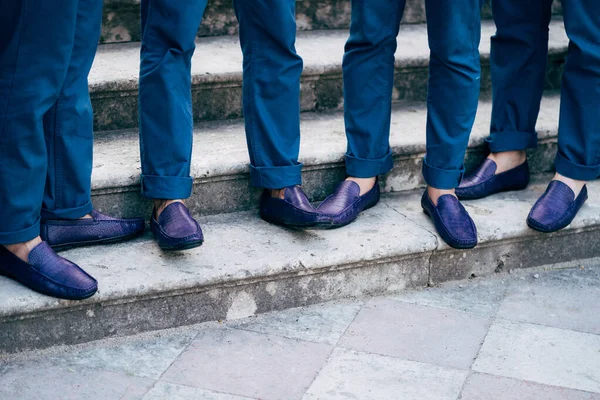 Seven grooms best men in identical blue trousers and shoes stand on the stairs, close-up