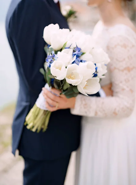 The bride and groom stand hugging and hold a wedding bouquet with white and blue flowers and eucalyptus branches close-up — Foto Stock