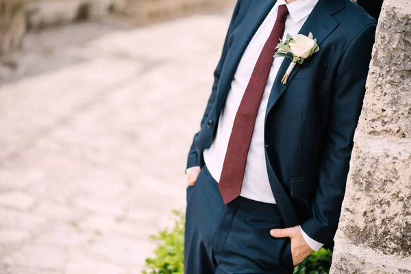 The groom in the suit with a red tie and a boutonniere with white rose on the street of the old town, close-up – stockfoto