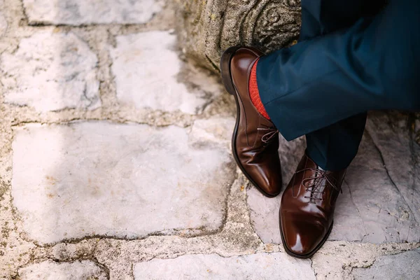 Crossed legs of a man in blue pants, red socks and brown shoes standing on the stone road, top view — Fotografia de Stock