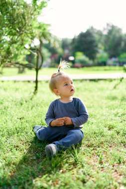 At kuyruklu çocuk yeşil çimlerde ağzı açık oturur.