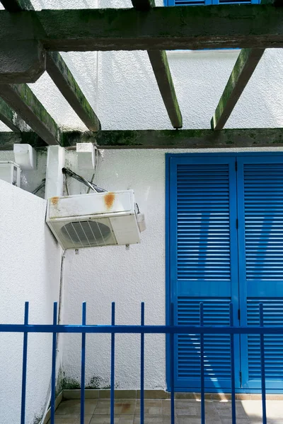 Klimatyzator wisi na białej ścianie domu w pobliżu niebieskich drzwi — Zdjęcie stockowe