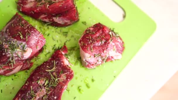 Bitar av rå biff på en grön skärbräda, beströdda med salt och rosmarin, hälls med solrosolja. — Stockvideo