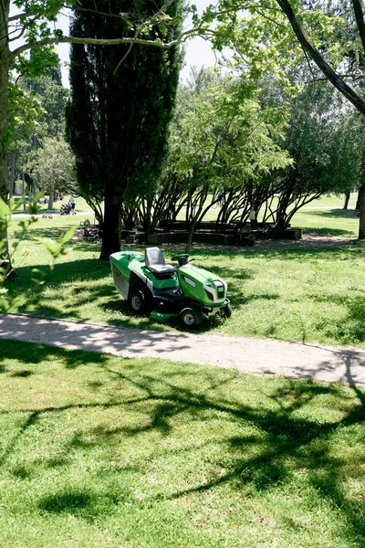 Motorized large green lawn mower stands near the trees in the park — Stock Photo, Image