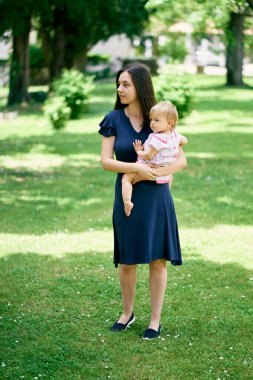 Annem yeşil bir parkta kollarında küçük bir kızla duruyor.