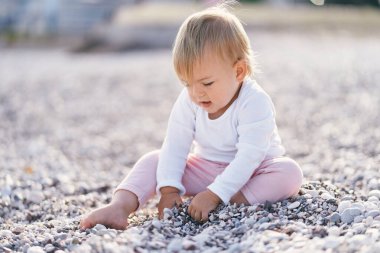 Çocuk çakıl taşı plajında oturur ve küçük çakıl taşları kazar.