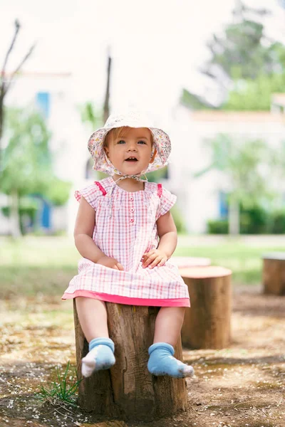 帽子をかぶった女の子が木の切り株に座って — ストック写真