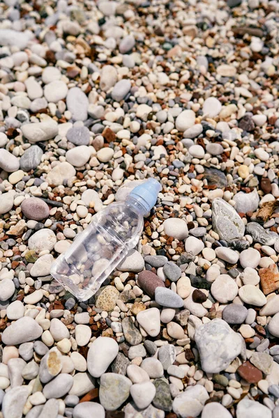 Small bottle of water lies on a pebble beach. View from above