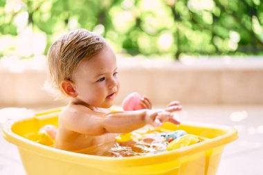 Çocuk elinde ördekle su ve oyuncak dolu bir kasede oturuyor.