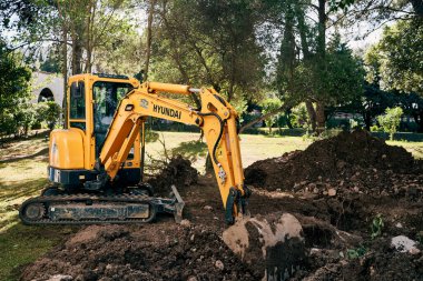 Yellow excavator digs the ground in a green park clipart