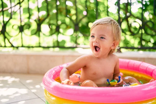 Bambino ridente si siede in una piccola piscina gonfiabile con giocattoli — Foto Stock