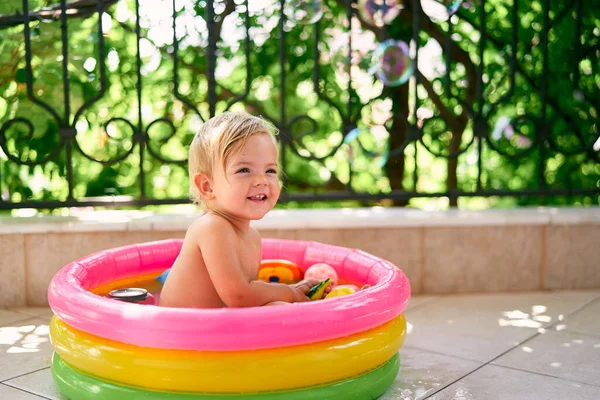 Bambino bagnato sorridente seduto in una piccola piscina gonfiabile con giocattoli — Foto Stock