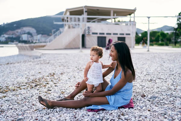 Ibu dengan seorang gadis kecil duduk di pantai kerikil di tepi laut — Stok Foto