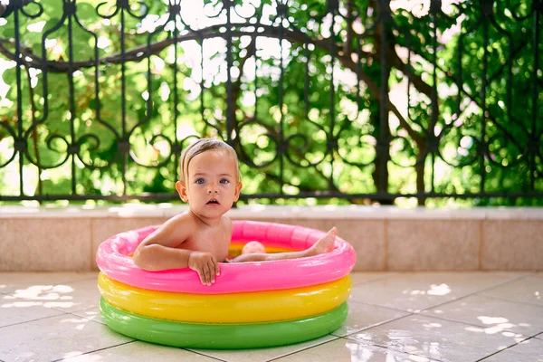 Bambino carino seduto in una mini piscina gonfiabile che tiene i lati — Foto Stock