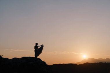 Gelinin silueti gün batımında dağın tepesinde duruyor.