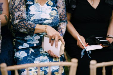 Elbiseli kadınlar çimenlikteki sandalyelerde otururlar ve davetiyeler kurdelelerle süslenir.