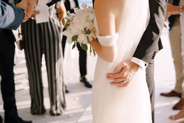 Sposo abbraccia sposa con un bouquet mentre in piedi di fronte agli ospiti — Foto Stock