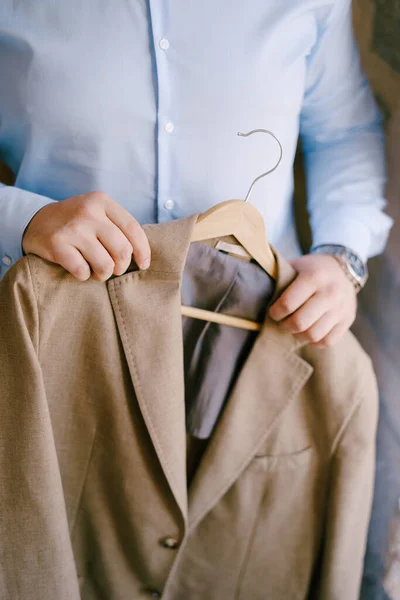 Novio en una camisa azul sostiene una chaqueta marrón en una percha —  Fotos de Stock