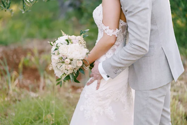 Bruid knuffels bruidegom met een boeket bloemen in de natuur — Stockfoto