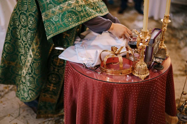 Kněz stojí před svatebním stolem s korunami, svíčkami a biblí — Stock fotografie