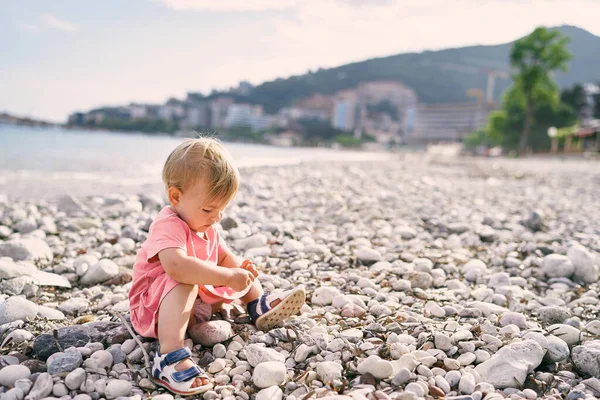 Gadis kecil duduk di pantai kerikil dan bermain dengan kerikil — Stok Foto